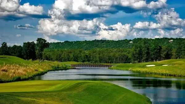Un campo de golf sereno con un sinuoso obstáculo de agua, calles verdes exuberantes y cielo azul nublado.