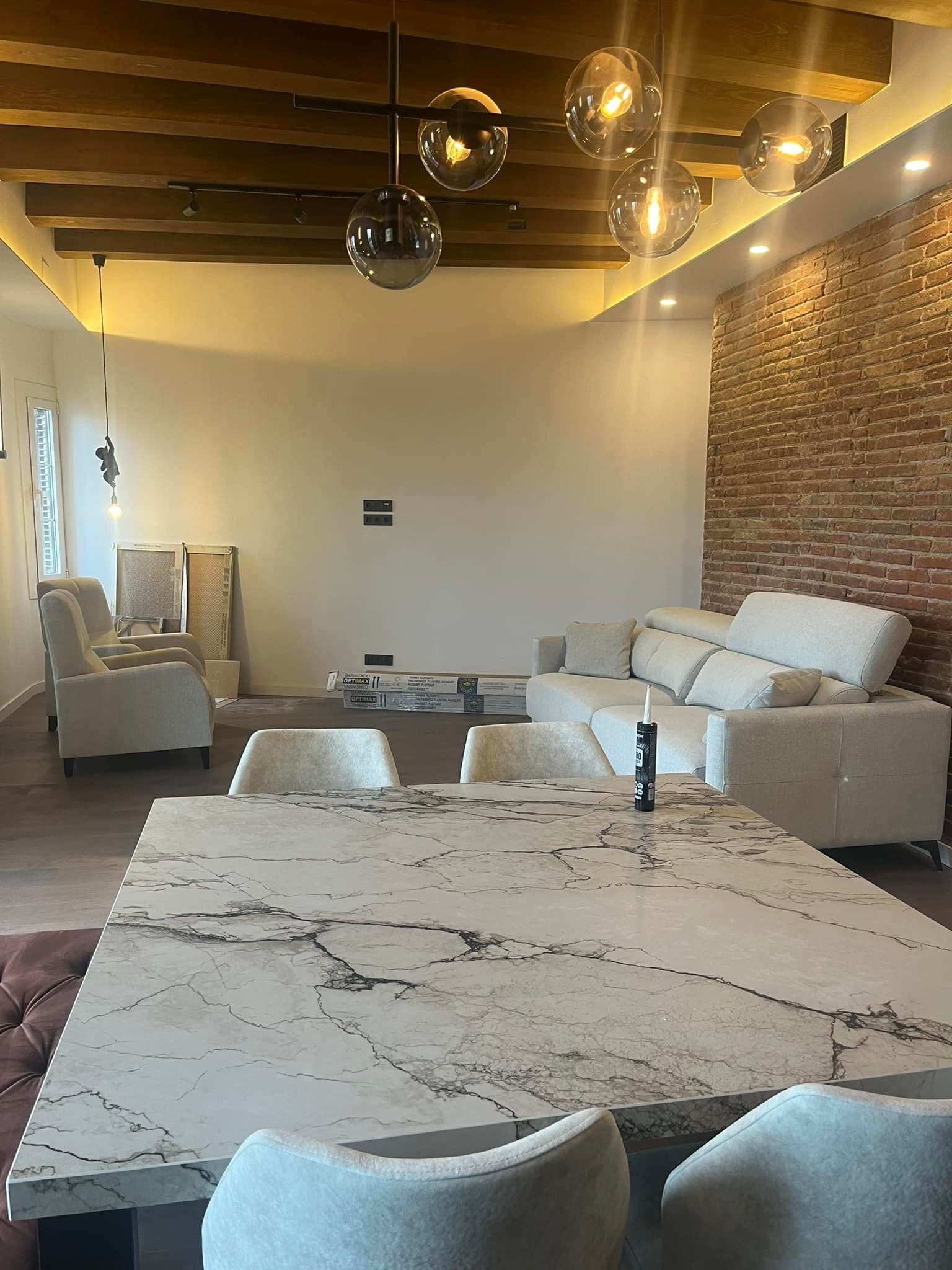 Comedor con mesa grande, sillas y sofá color blanco roto contra una pared de ladrillo.