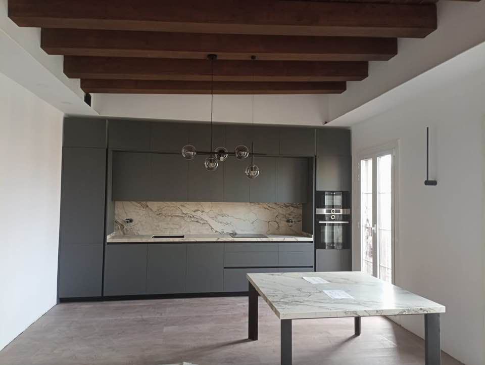 Cocina gris moderna con encimeras de mármol, vigas de madera en el techo y mesa de comedor a juego.