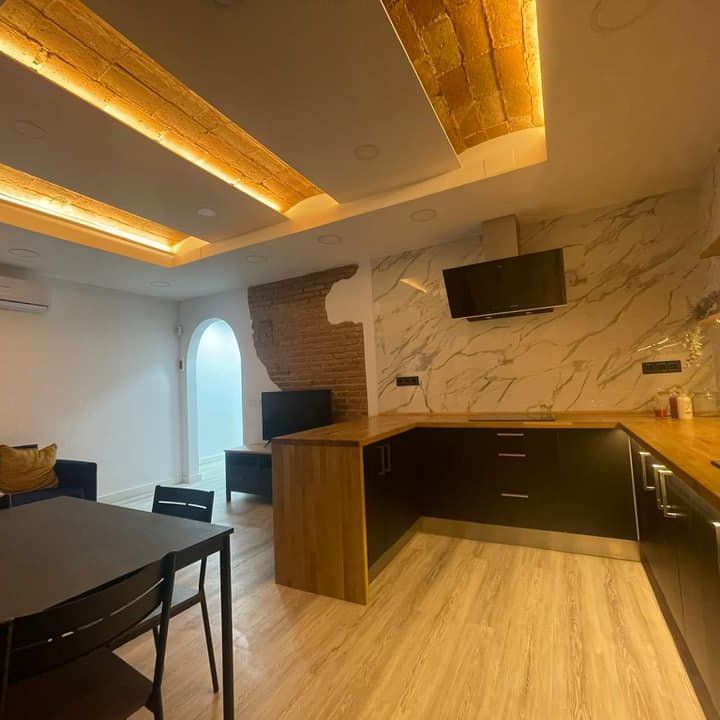 Cocina moderna con salpicadero de mármol, gabinetes de madera y una mesa negra.