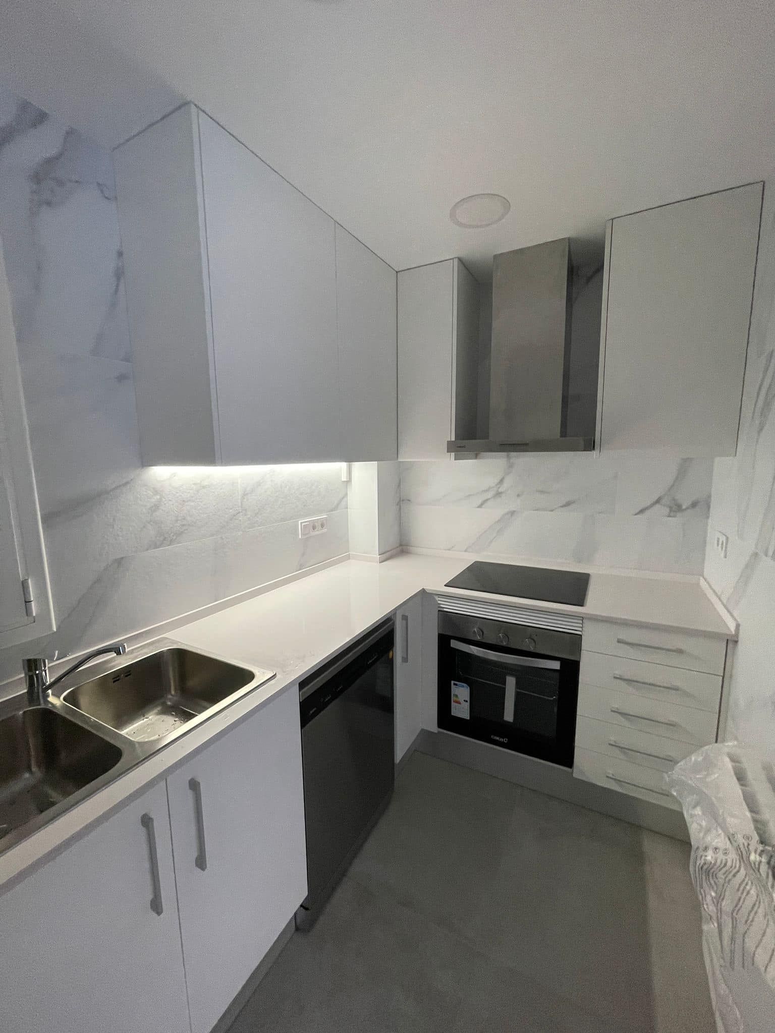 Cocina moderna blanca con salpicadero y encimeras con diseño de mármol. Electrodomésticos incluidos: horno, estufa y fregadero.