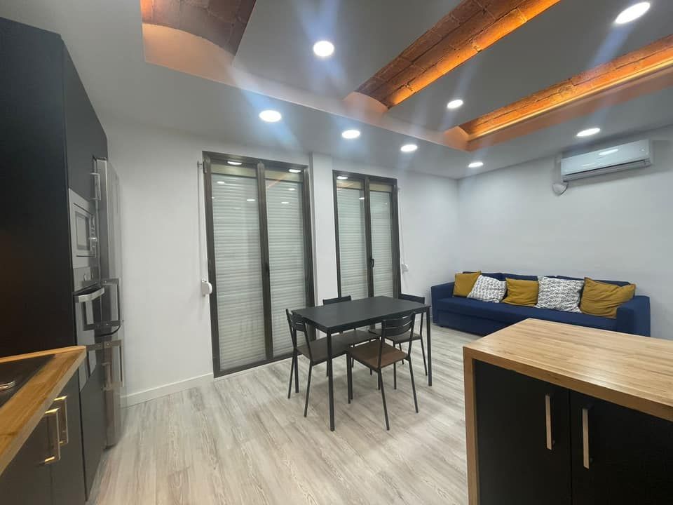 Moderna sala de estar con cocina, comedor y sofá azul. Incluye armarios oscuros y puertas corredizas de cristal.