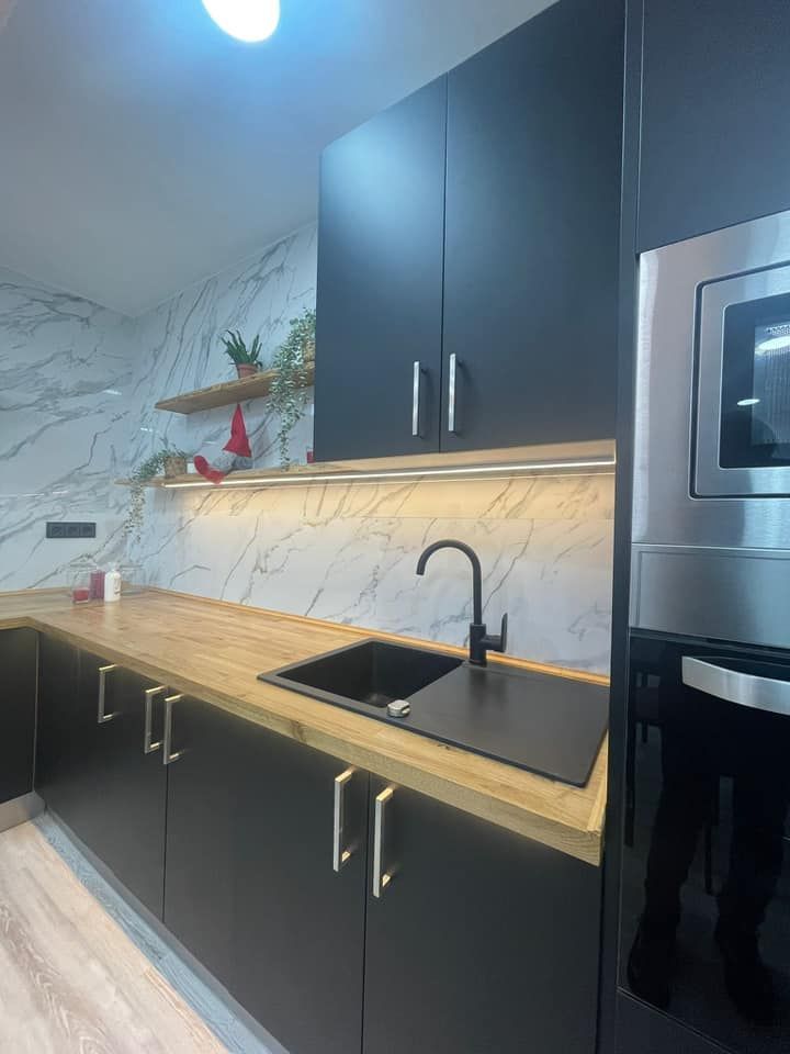 Cocina moderna con gabinetes negros, encimera de madera y protector contra salpicaduras de mármol.