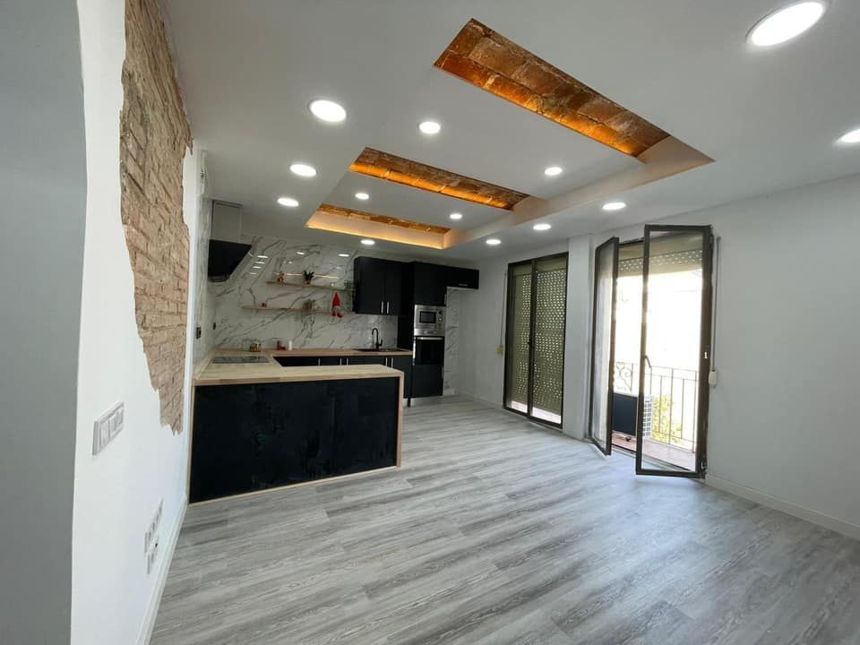 Interior de apartamento moderno renovado con pared de ladrillo a la vista, cocina oscura y luces de techo con paneles de madera.