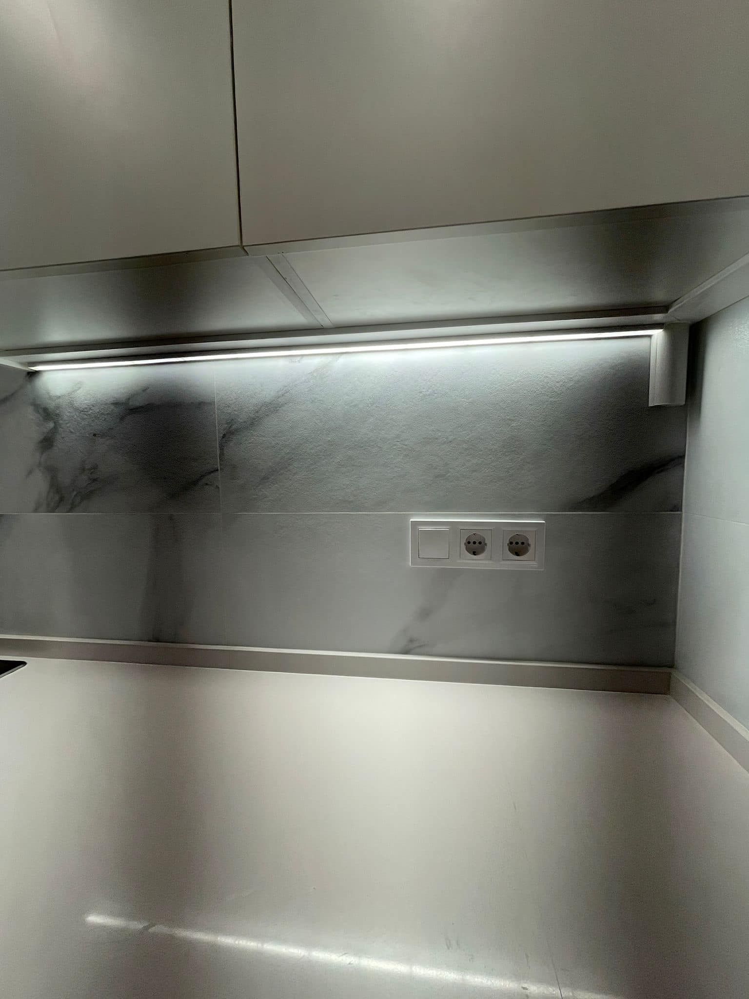Cocina blanca con protector contra salpicaduras y tiras de iluminación que iluminan la encimera y los enchufes.