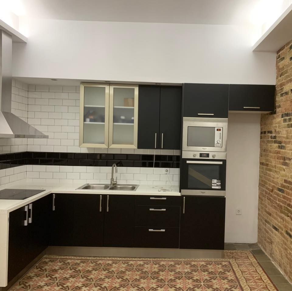 Cocina moderna con gabinetes negros, encimeras blancas y pared de ladrillo.