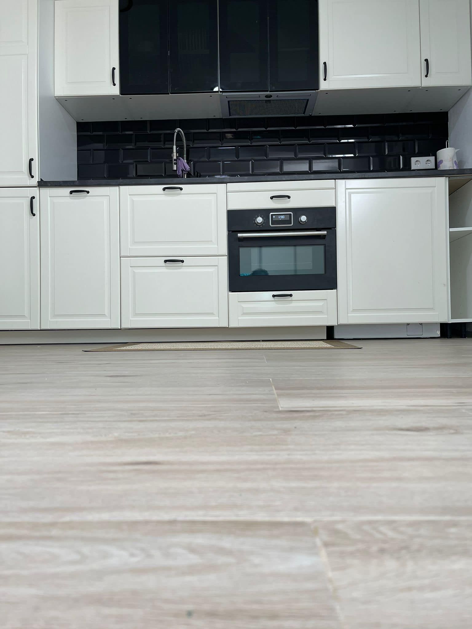 Gabinetes de cocina blancos con detalles en negro, protector contra salpicaduras negro y pisos con apariencia de madera clara.