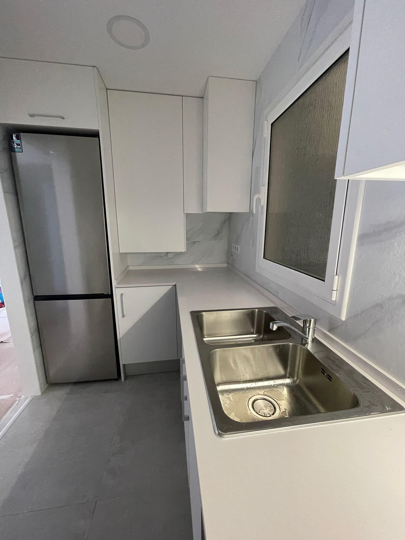 Cocina blanca con electrodomésticos de acero inoxidable y fregadero.