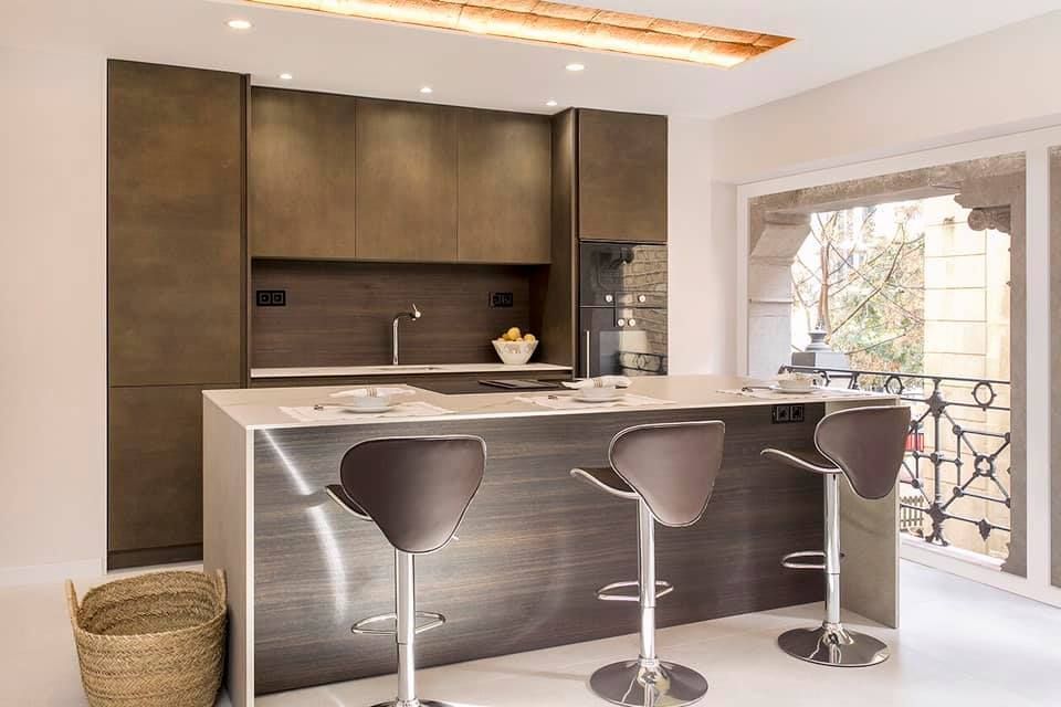 Cocina moderna con gabinetes marrones, isla con taburetes de bar y luz desde la ventana.