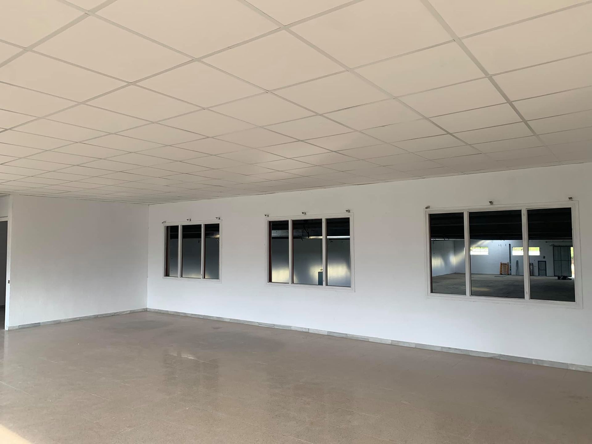 Habitación blanca vacía con tres ventanas. Suelo beige, paredes y techo blancos.