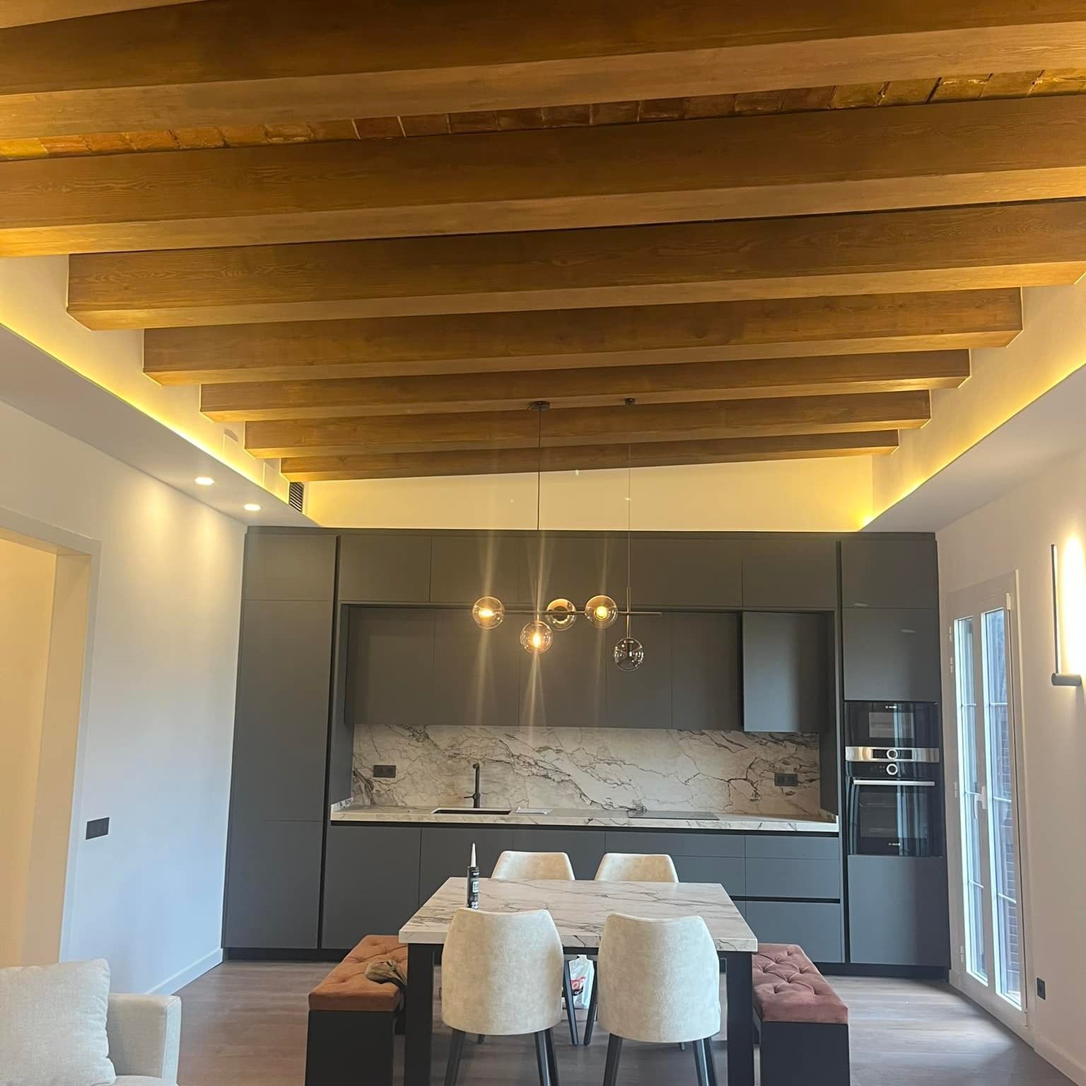 Cocina moderna con gabinetes de color gris oscuro, salpicadero de mármol y vigas de madera en el techo.