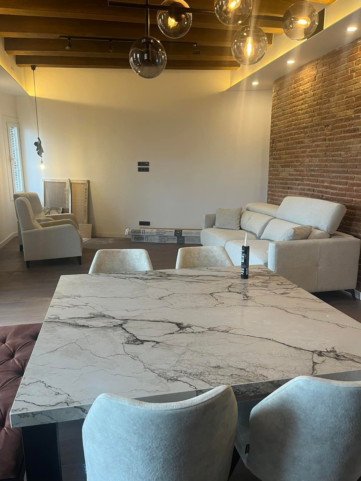 Comedor formal con mesa grande de mármol, asientos lujosos y pared con detalles de ladrillo.