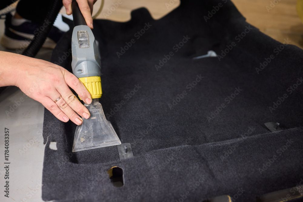 Eine Person reinigt einen schwarzen Autoteppich mit einem Dampfreiniger.