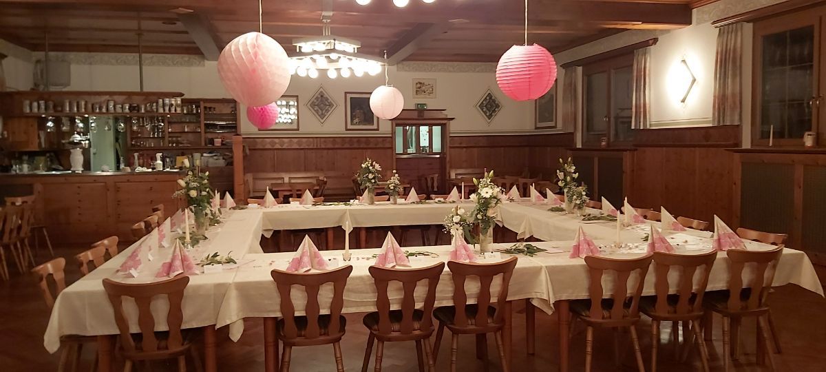 Ein schön dekoriertes Restaurant mit einem quadratischen Tisch, der für eine Feier gedeckt ist. Von der Decke hängen rosa Papierlaternen.
