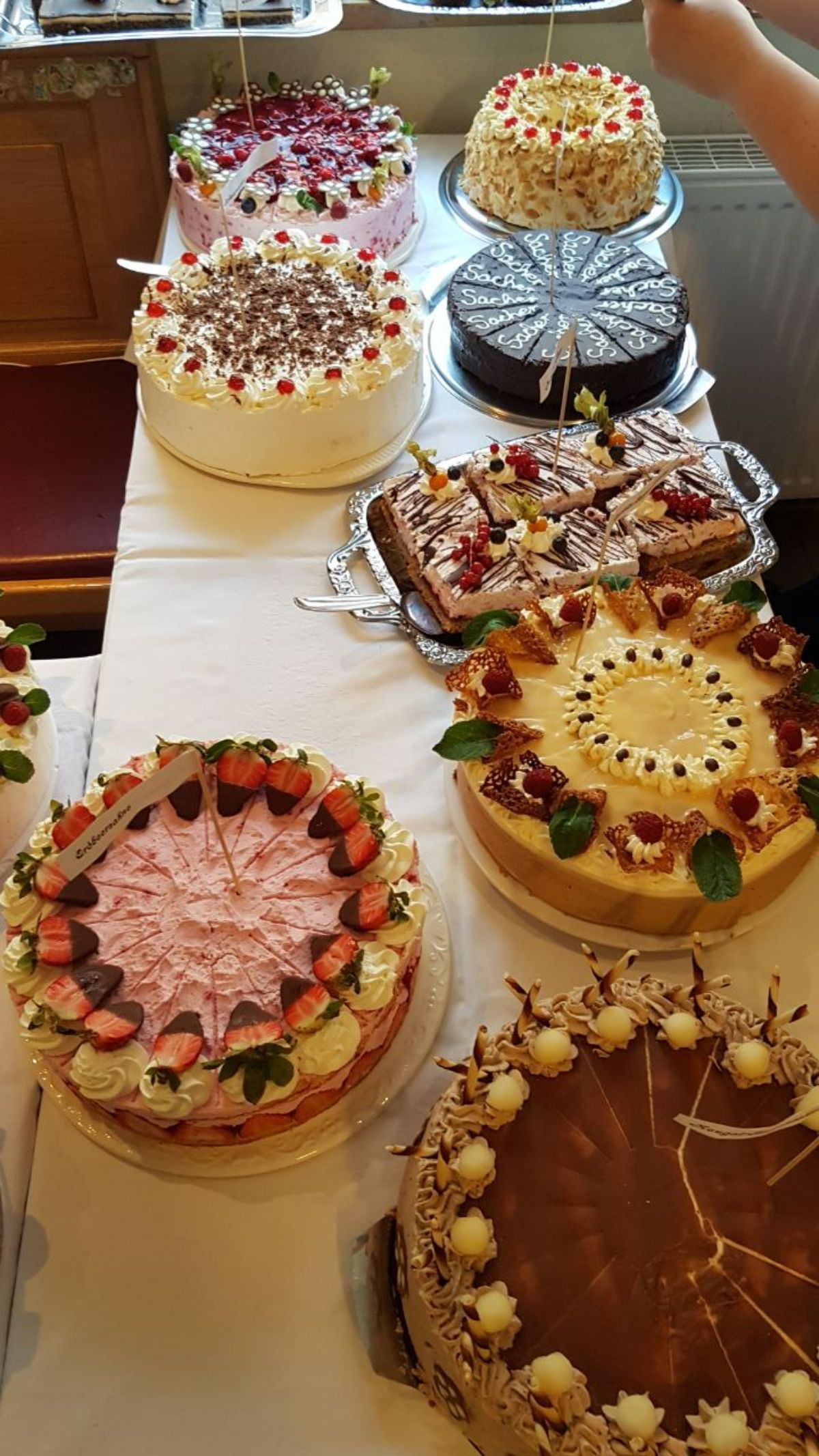 Verschiedene dekorierte Kuchen auf einer weißen Tischdecke, möglicherweise eine Dessertpräsentation auf einer Party.