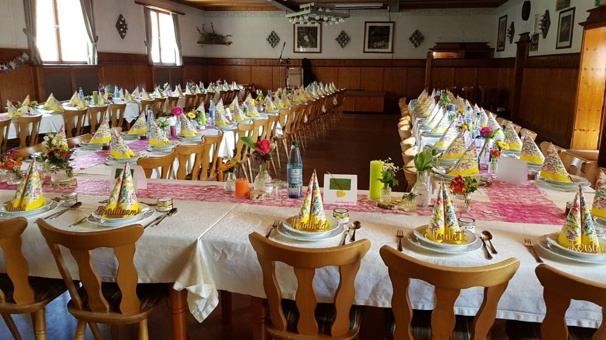 Lange, für eine Party gedeckte Tische, Holzstühle, weiße Tischdecken, Dekorationen und Partyhüte.