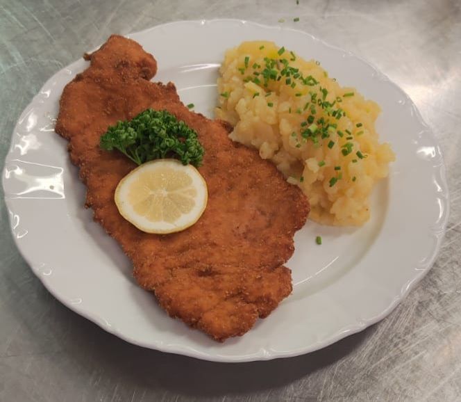 Paniertes Schnitzel mit Kartoffelpüree und Zitronengarnitur auf einem weißen Teller.