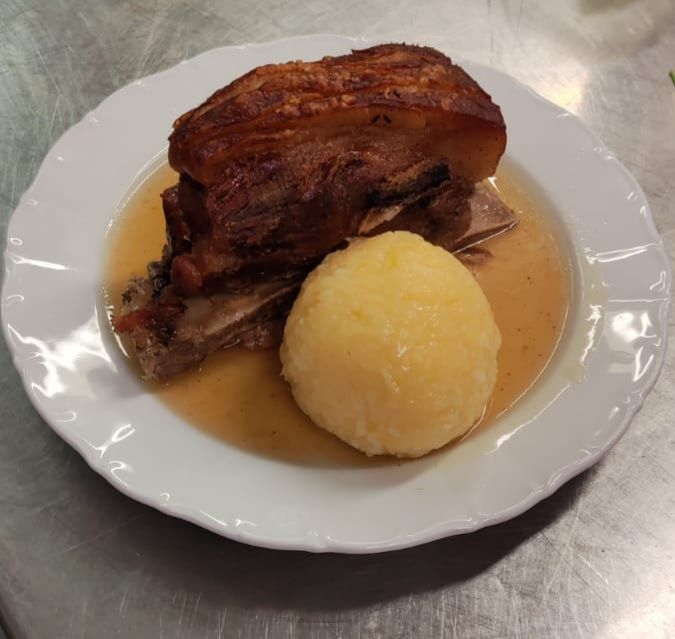 Gebratene Schweineschulter mit knuspriger Haut und Kartoffelknödel auf einem weißen Teller, in Soße.