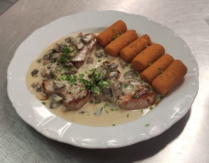 Schweinemedaillons in Champignon-Sahnesauce mit frittierten Kroketten, serviert auf einem weißen Teller.