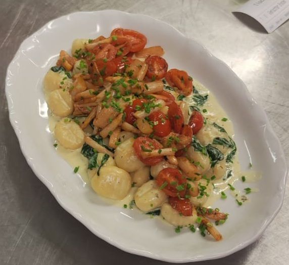 Gnocchi-Gericht mit Tomaten, Champignons und Spinat in einer cremigen Sauce, garniert mit Schnittlauch.