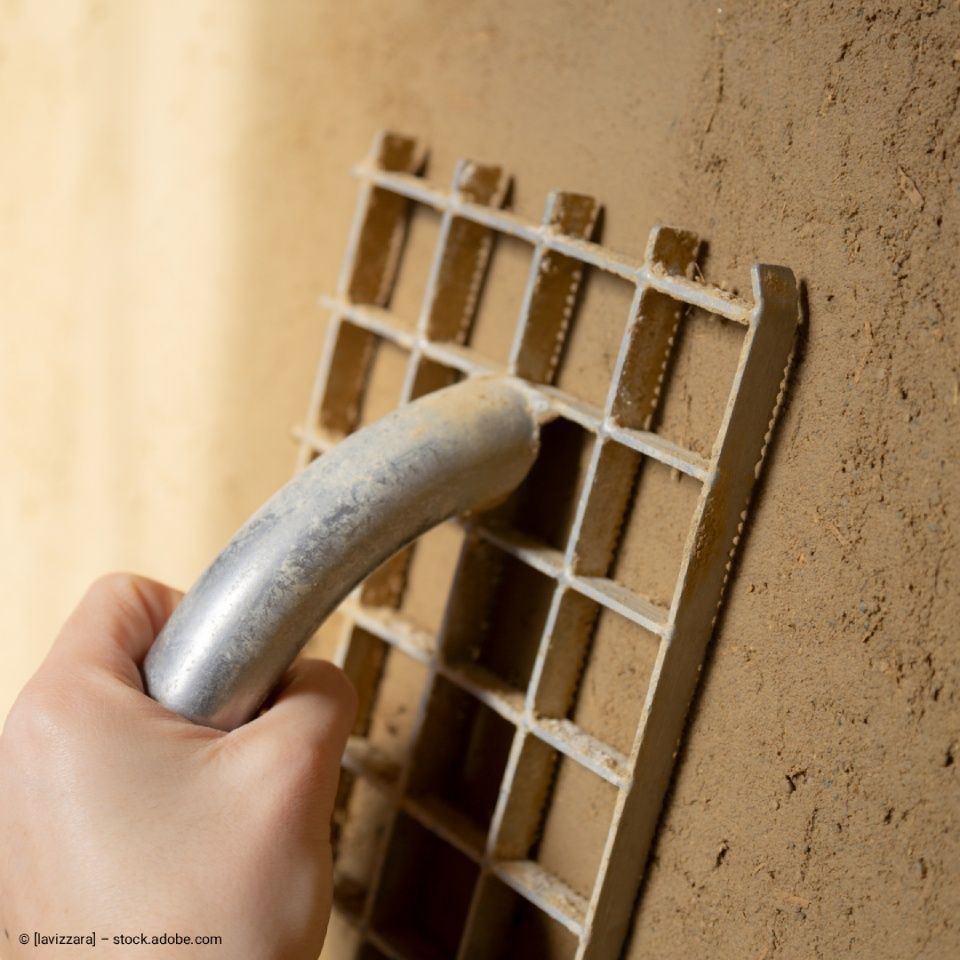 Eine Hand hält eine Kelle mit grünem Griff und verteilt etwas auf einer braunen Oberfläche.