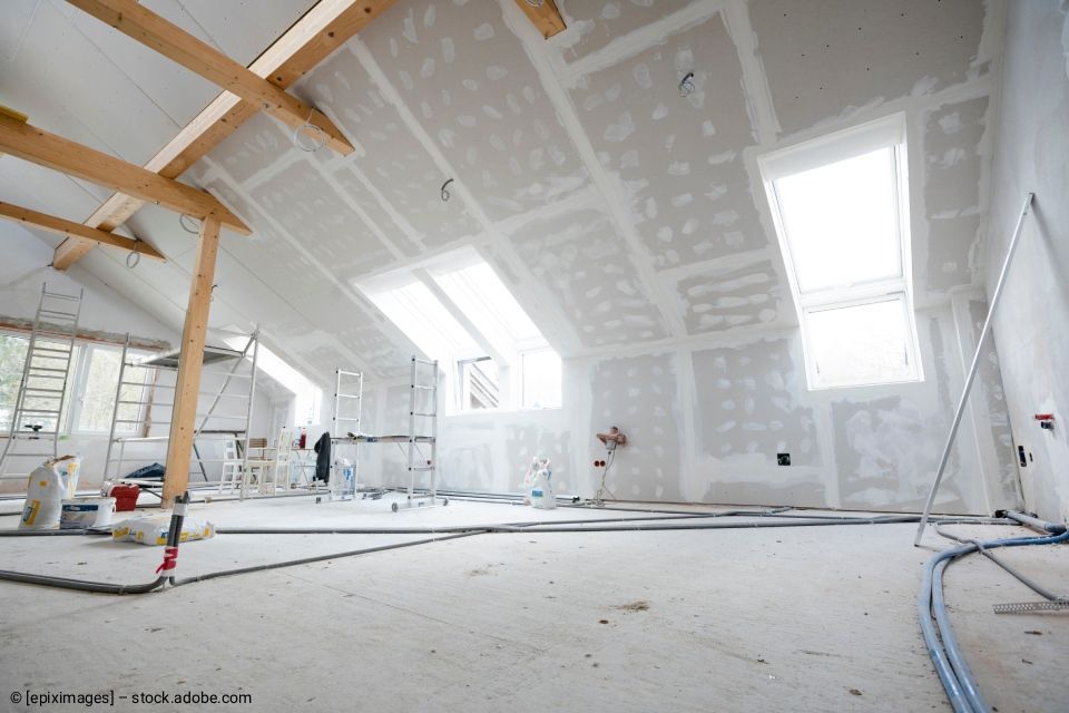 Innenansicht eines im Bau befindlichen Raumes mit Gipskartonwänden, freiliegenden Balken, Oberlichtern und Werkzeugen.