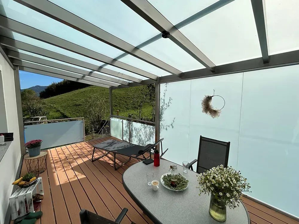 Eine Terrasse mit Tisch und Stühlen unter einem Glasdach
