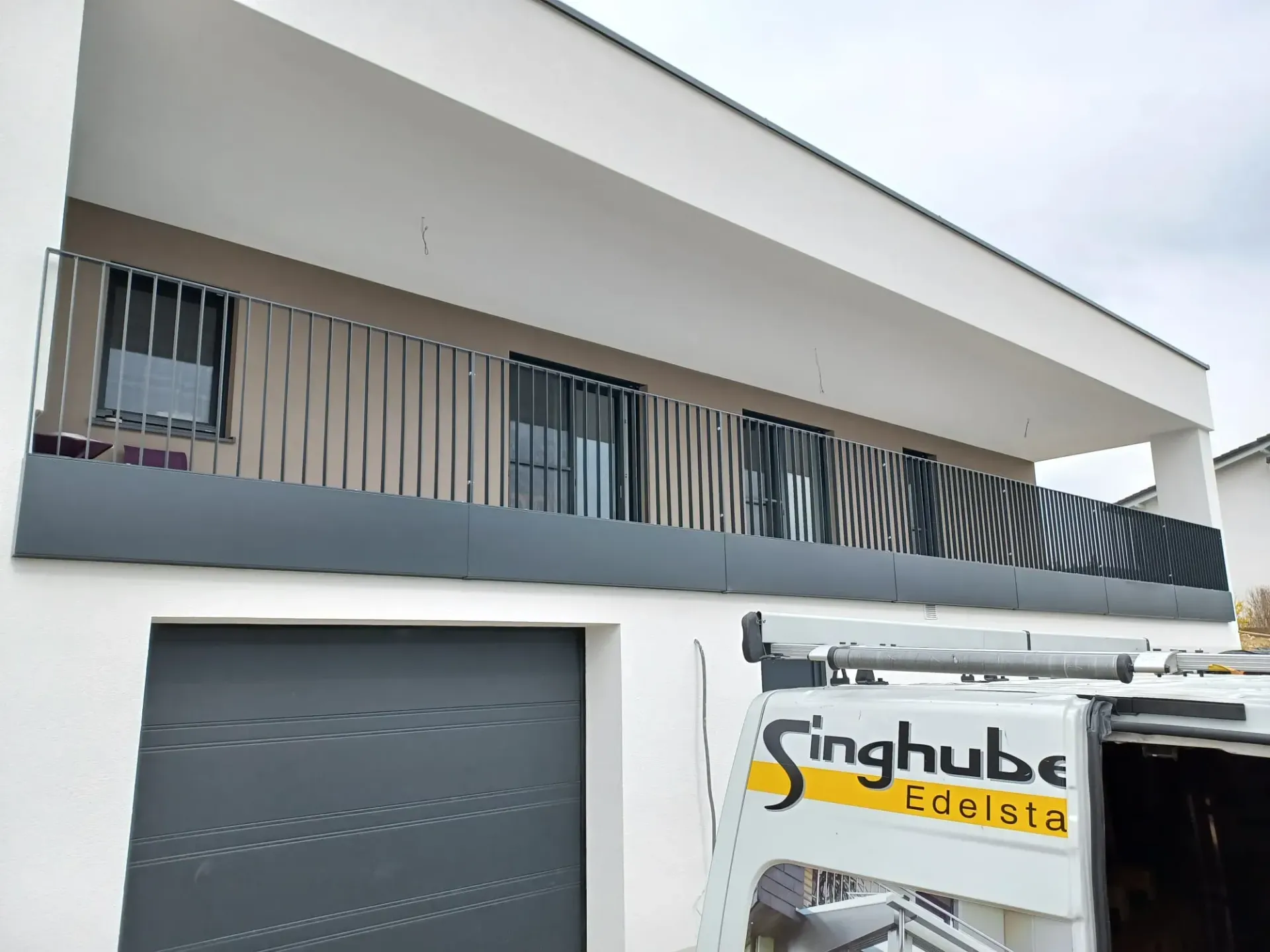 Ein weißer Lieferwagen parkt vor einem Haus mit Balkon.