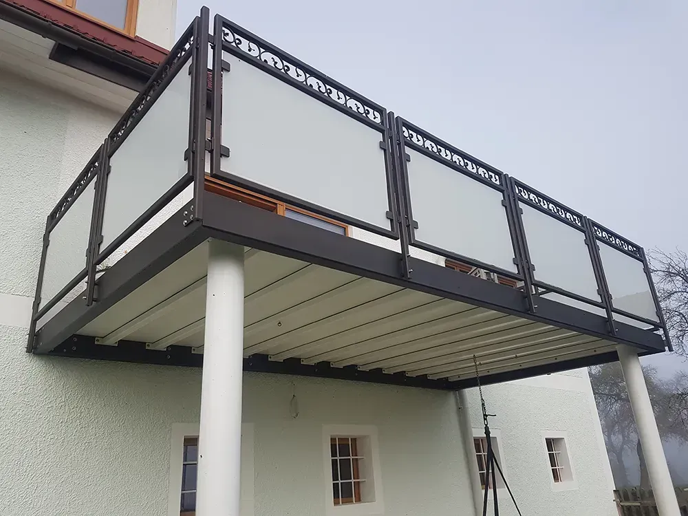 An der Seite eines Hauses befindet sich ein Balkon mit Glasgeländer.