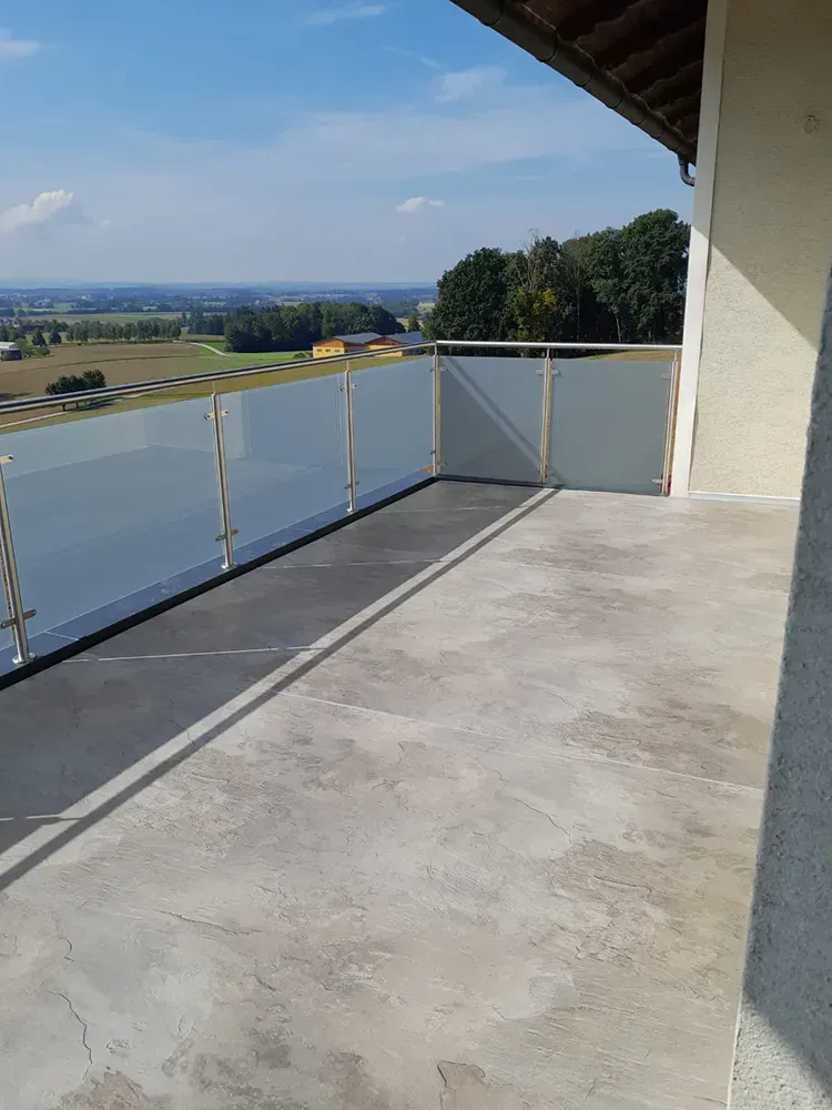 Ein Balkon mit Glasgeländer und Blick auf ein Feld.