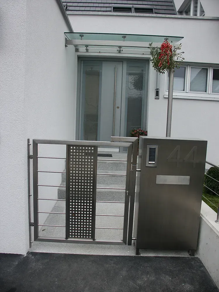 Ein Briefkasten aus Edelstahl steht vor einem weißen Haus