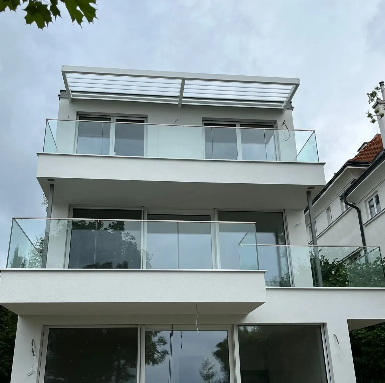 Ein weißes Haus mit Glasbalkons und einem Vordach