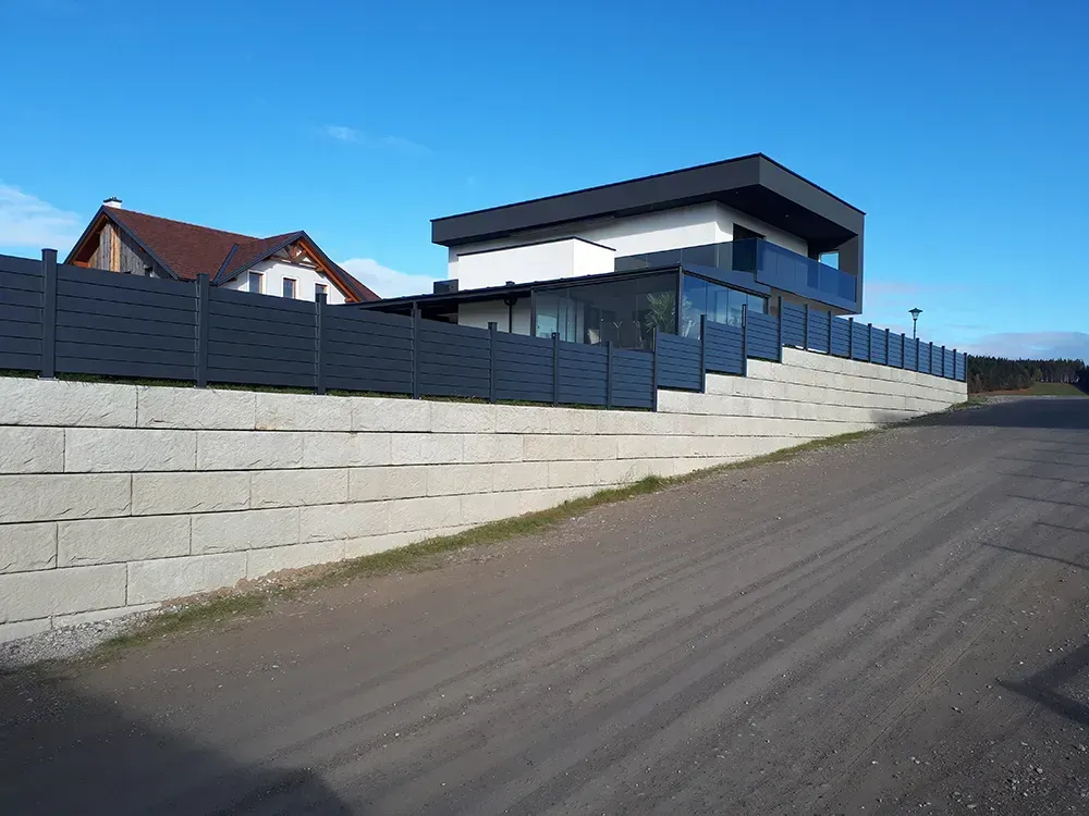 Auf einem Hügel neben einer unbefestigten Straße steht ein eingezäuntes Haus.