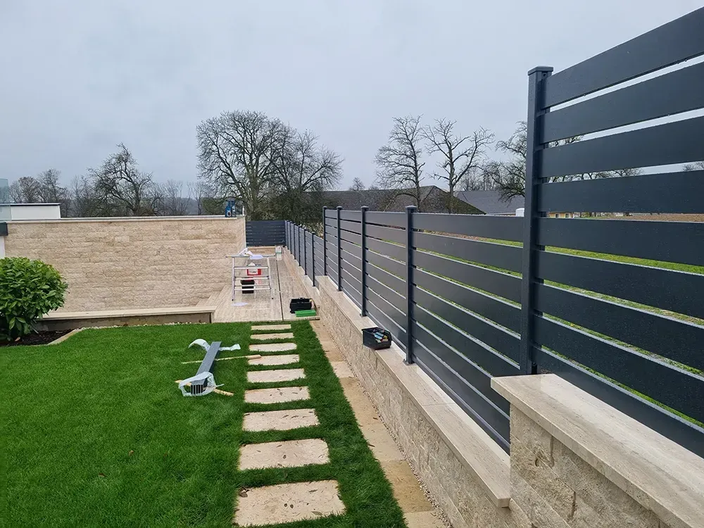 Ein schwarzer Zaun umgibt einen üppig grünen Hof.