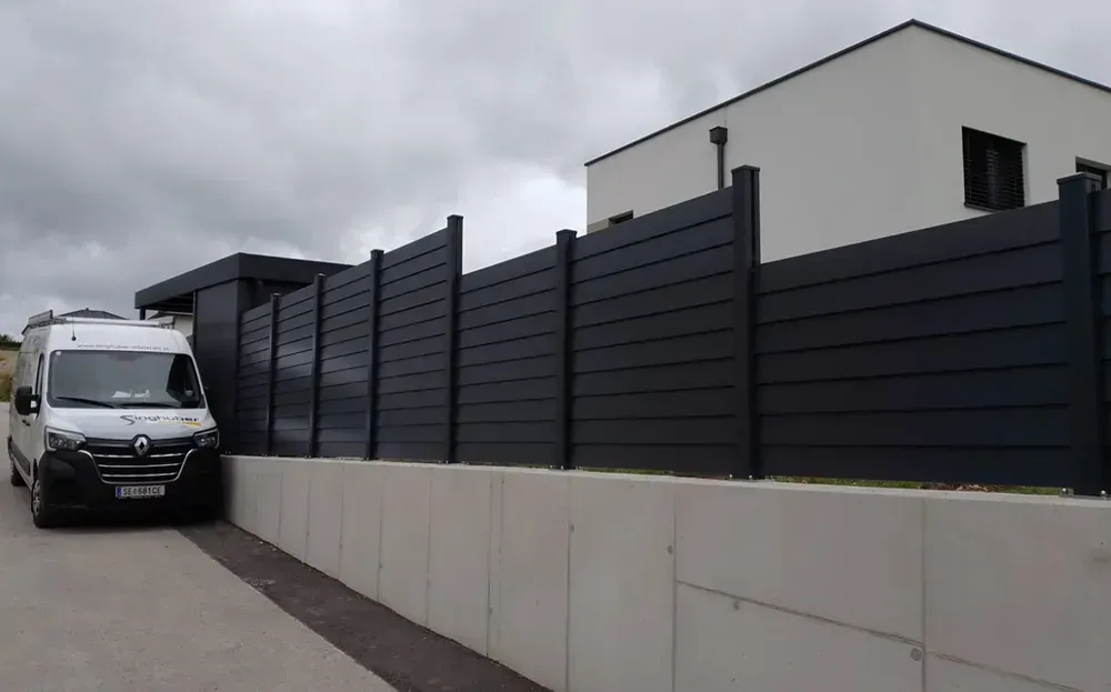 Ein weißer Lieferwagen parkt neben einem schwarzen Zaun vor einem Haus.