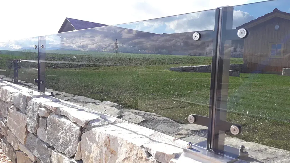 Eine Steinmauer mit einem Glasgeländer und einem Haus im Hintergrund.