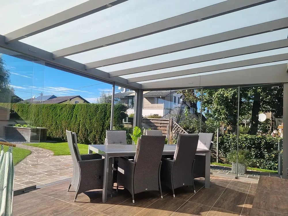 Eine Terrasse mit Tisch und Stühlen unter einem Glasdach.