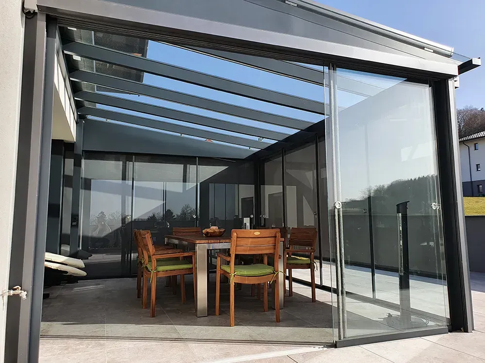 Eine Terrasse mit Tisch und Stühlen unter einem Glasdach.