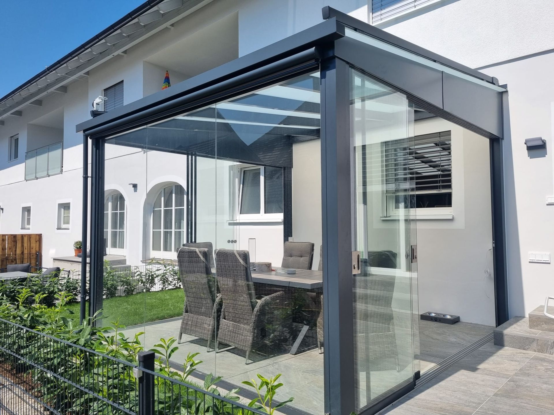 Eine Terrasse mit Tisch und Stühlen unter einem Glasdach.