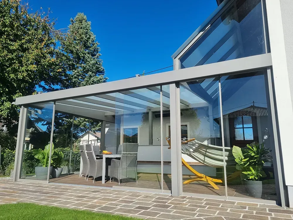 Eine Terrasse mit Tisch und Stühlen unter einem Glasdach