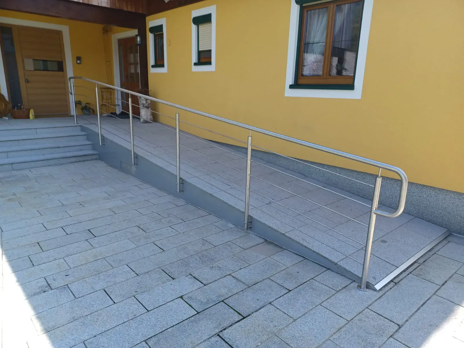 Eine Rampe mit einem Edelstahlgeländer vor einem gelben Haus