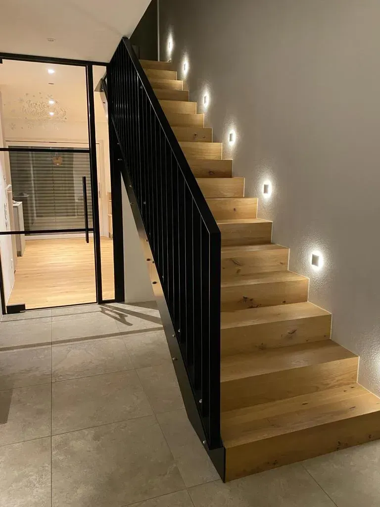 Eine Holztreppe mit schwarzem Geländer und Lichtern auf den Stufen.