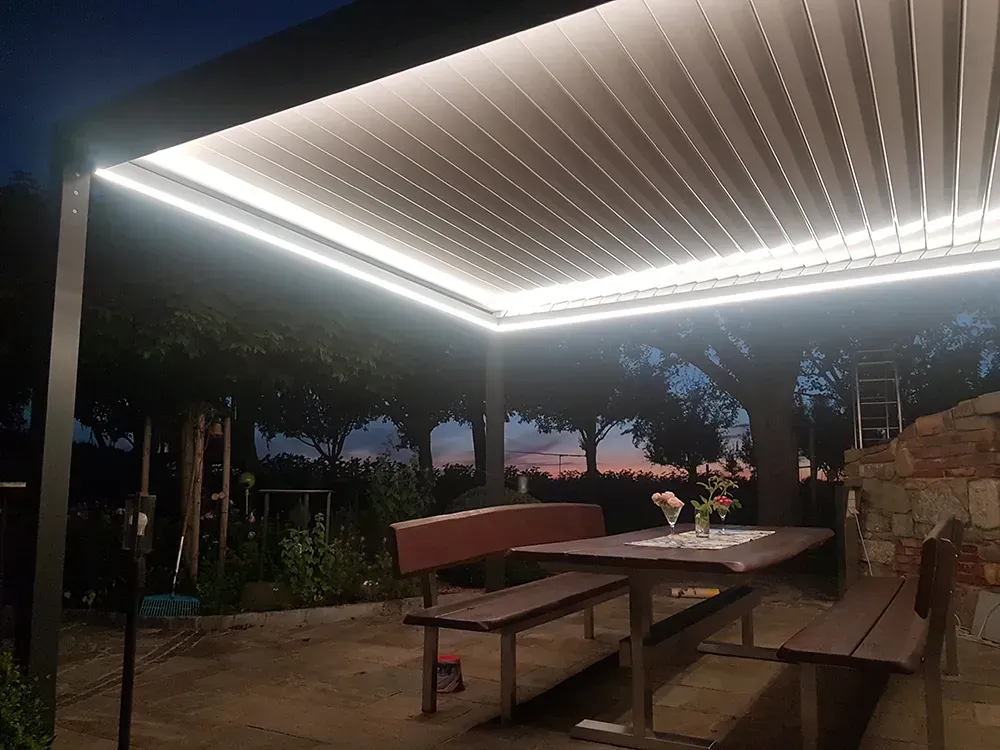 Eine Pergola mit einem Tisch und Bänken darunter für die Nacht.