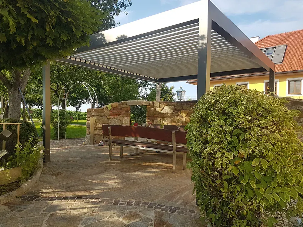 Eine Terrasse mit Pergola und Bank vor einem Haus.