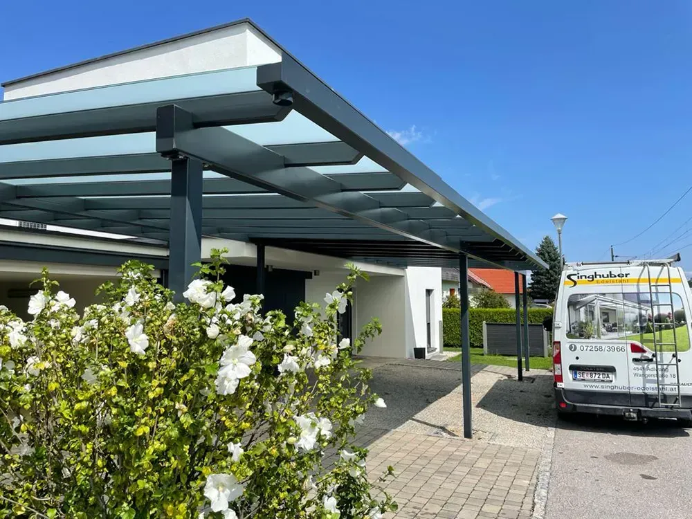 Ein weißer Lieferwagen steht unter einem Vordach vor einem Haus.