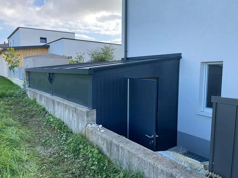 Neben einem weißen Haus steht ein schwarzer Schuppen.