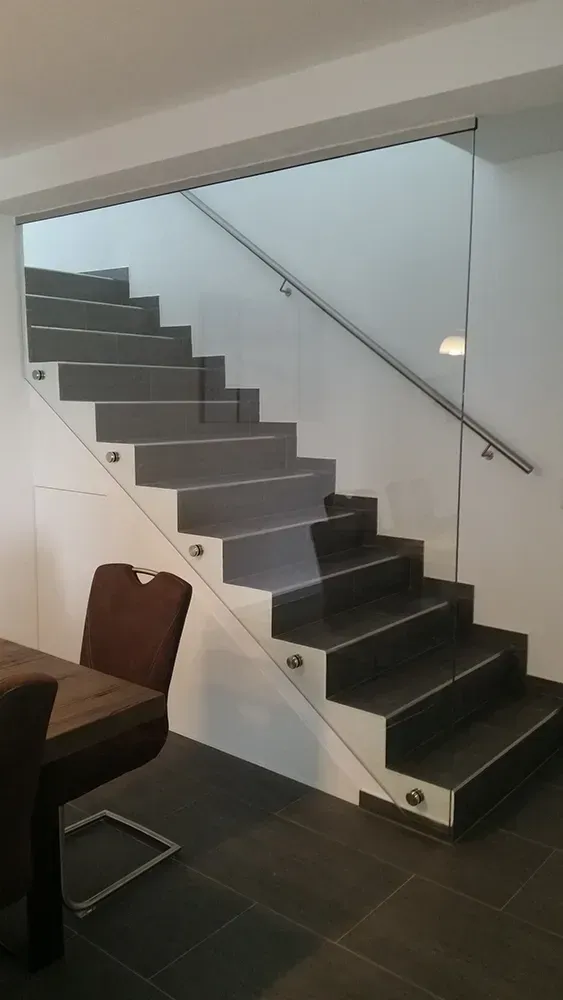 Eine Treppe mit Glasgeländer in einem Esszimmer mit Tisch und Stühlen.