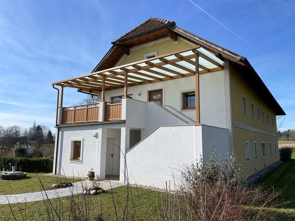 Ein großes gelb-weißes Haus mit einem Balkon und einer Pergola.