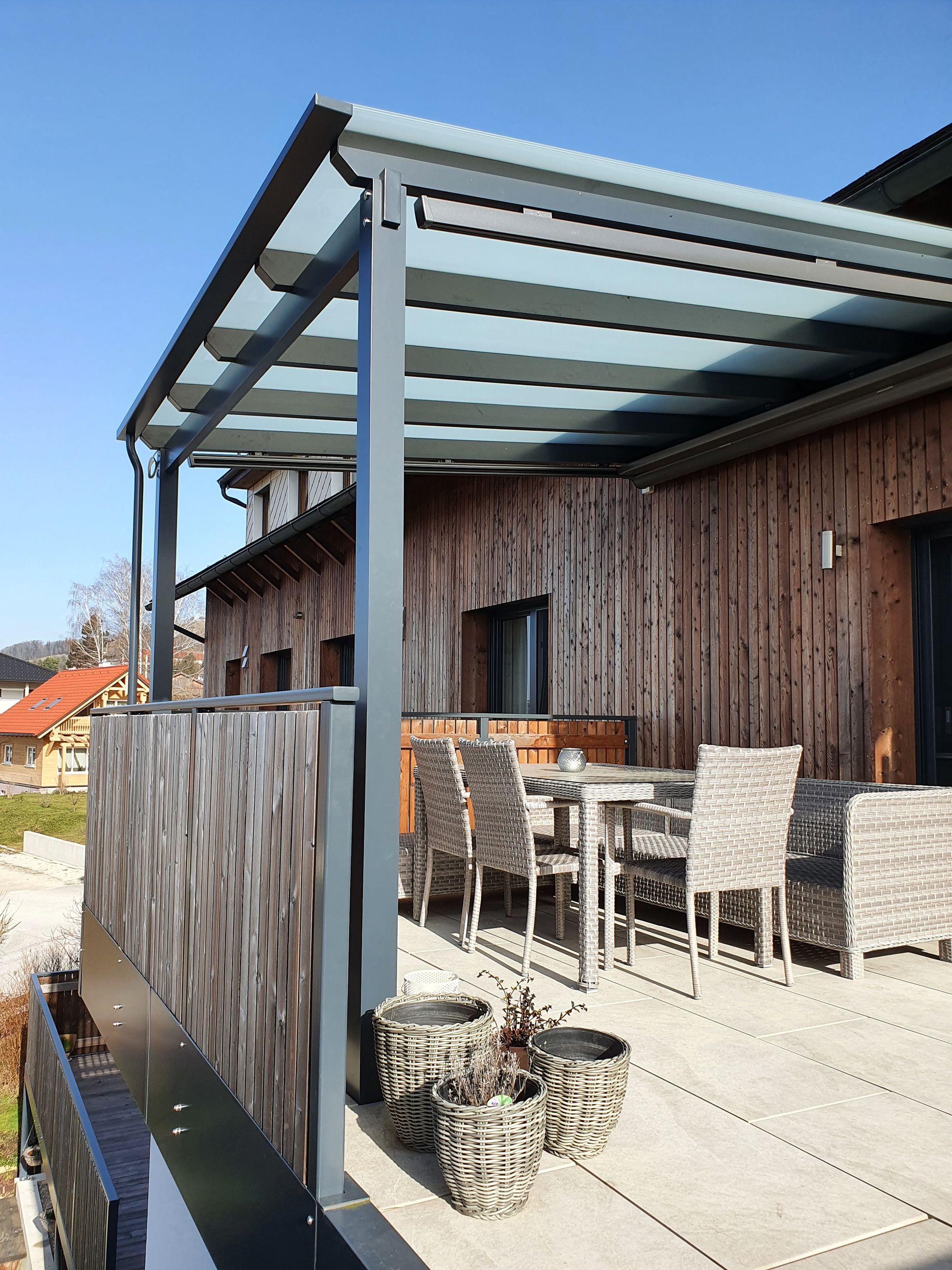 Eine Terrasse mit Tisch und Stühlen unter einem Glasdach.