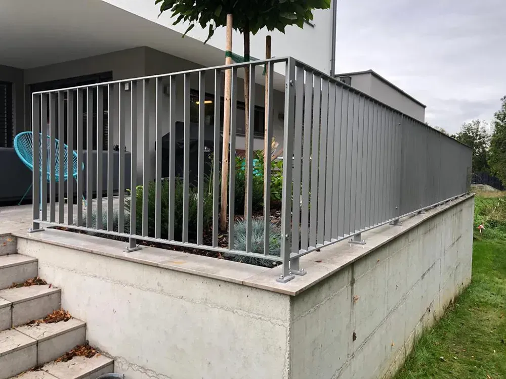 Auf einer Betonmauer neben einer Treppe steht ein Metallzaun.